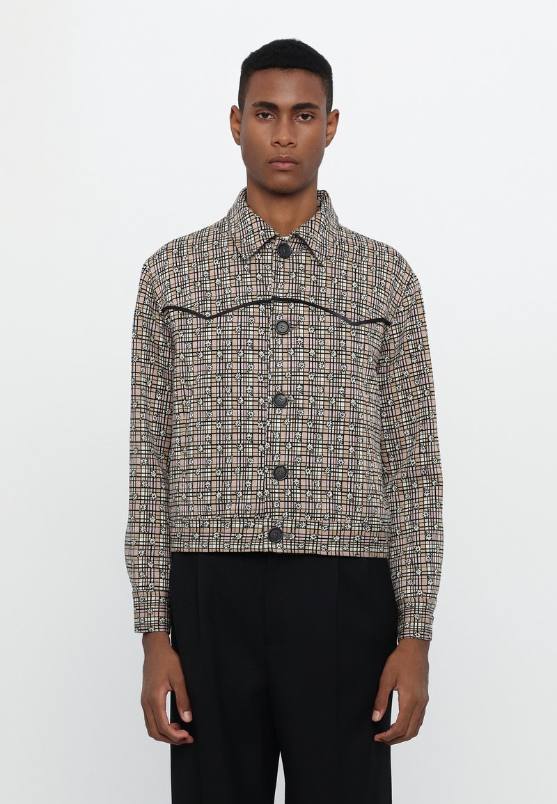 Brown checkered jacket with black accents and button closure. Features a collared neck and cropped design, made from textured fabric.