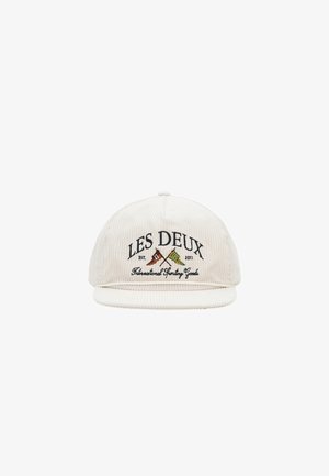 Casquette en velours côtelé écru avec le texte brodé "LES DEUX" et des drapeaux croisés. Elle présente une visière plate et un tissu texturé pour plus de profondeur.