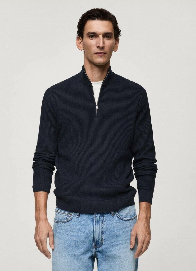 Navy ribbed sweater with a zippered collar, long sleeves, and a fitted waist, worn over light blue denim jeans. Textured knit fabric.