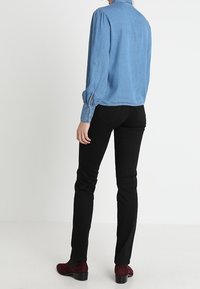 Ljusblå denimblus med rynkade ärmar, kombinerad med svarta tajta byxor och vinröda ankelstövlar. Enkel design med en klassisk silhuett.