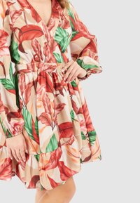 Abito con stampa floreale che presenta foglie rosse e verdi su uno sfondo beige. Ha una profonda scollatura a V, maniche lunghe a sbuffo e una gonna a strati.