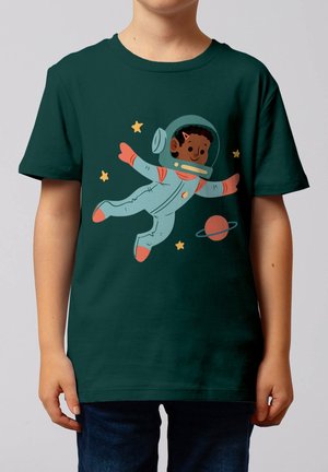 Kind trägt dunkelgrünes Shirt mit Illustration eines lächelnden Astronauten, der zwischen Sternen und einem Planeten mit Ringen schwebt.