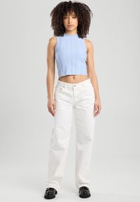 Light blue ribbed knit crop top with a high neckline paired with white wide-leg pants and black ankle boots. Textured and tailored fit.