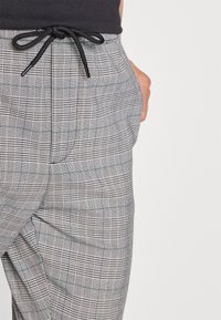 Šedé kostkované kalhoty s páskem na stažení, kombinující černé a bílé vzory s akcenty zelené.