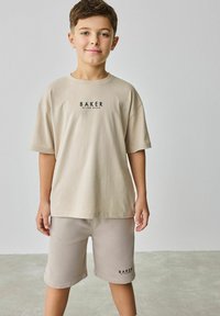 Beige bavlněné tričko s logem "BAKER" na hrudi, spárované s odpovídajícími béžovými šortkami, které mají volný střih a hladkou texturu.