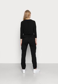 Musta pitkähihaista paita ja mustat cargo-housut joustavilla hmanteilla, molemmat pehmeää materiaalia. Valkoiset lenkkikengät täydentävät asun.