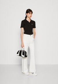 Polo nero, jeans bianchi svasati e una borsa in bianco e nero. Le scarpe sono bianche con dettagli neri. Design semplice con dettagli minimi.