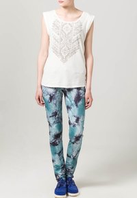 Haut sans manches blanc avec un léger motif géométrique ; pantalons bleu tie-dye ; chaussures bleues avec semelles blanches. Design simple avec un tissu texturé.