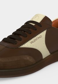 Baskets en cuir marron avec lacets marron foncé et panneau latéral blanc avec le logo Valentino en lettres marron foncé.