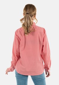 Camisa de manga larga a rayas rojas y blancas con puños abotonados, un yugo en la parte posterior y un dobladillo redondeado; combinada con vaqueros azules.
