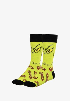 Yellow socks featuring a Grinch design, black cuff and toe, with repeated "Grinch" text in red and black, and green facial illustration.