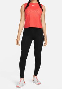 Punainen hihaton urheilupaita siksak-kuviolla, yhdistetty mustiin legginsseihin, joissa heijastavia yksityiskohtia, ja valkoiset lenkkarit, joissa on vaaleanpunaisia yksityiskohtia.