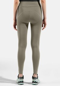 Leggings opachi verde oliva con vita alta, dettagli delle cuciture sul retro e una texture liscia e elastica. Indossati con sneakers nere e menta.