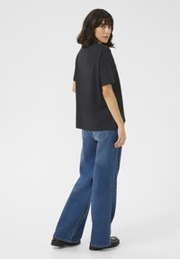 Schwarzes, übergroßes T-Shirt mit kurzen Ärmeln, kombiniert mit blauen, weit geschnittenen Jeans. Der Stoff wirkt weich und die Jeans haben eine klassische Denim-Struktur.