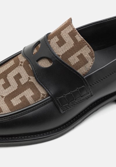 Tige en tissu brun à motifs avec des accents en cuir noir, présentant un design incurvé et un détail découpé sur la sangle. Semelle plate.