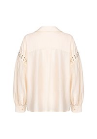 Blusa color crema con una vestibilità comoda, maniche lunghe a sbuffo e polsini con bottoni. Presenta grommet decorativi lungo le cuciture delle spalle.