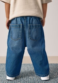 Modré rifle s elastickým pásom, so zadnými vreckami a voľným strihom. Tkanina má mierne vyblednutú textúru.