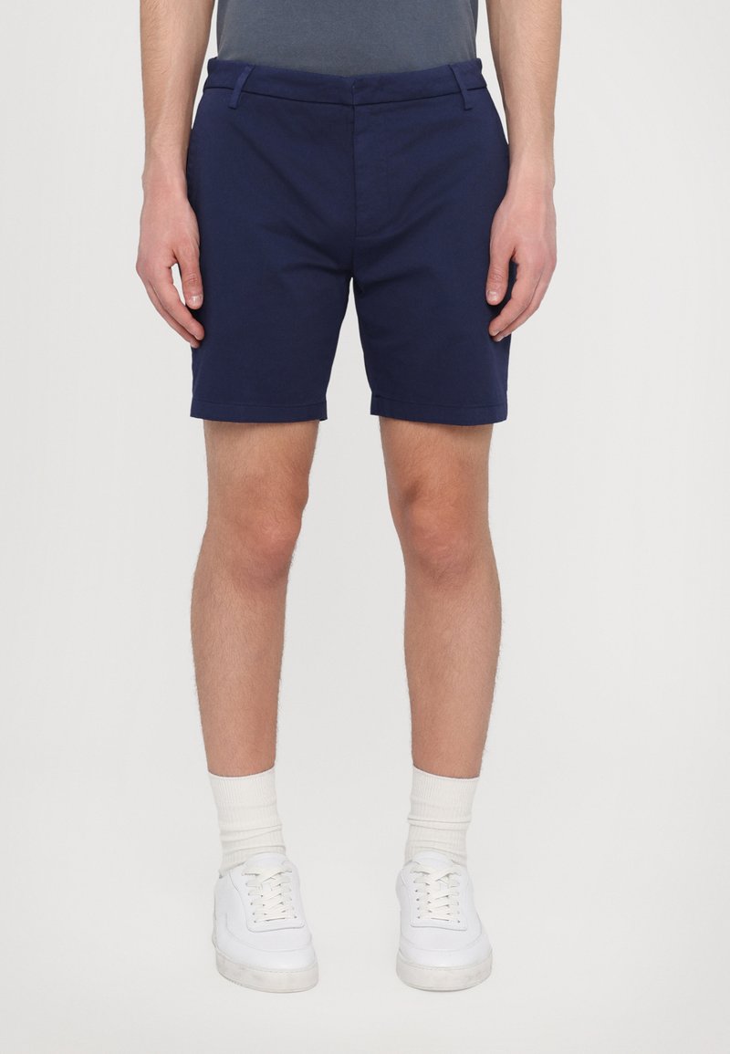 Pantaloni scurți bleumarin din bumbac, cu o croială dreaptă, buzunare din față plate și talie medie. Purtați cu teniși și șosete albe.