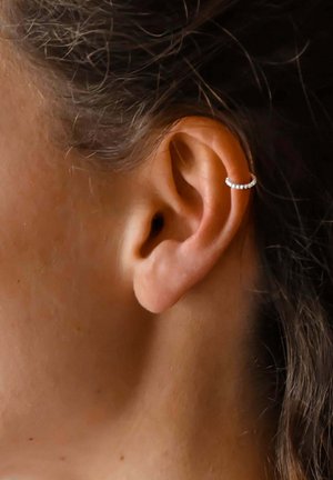 Orecchino a cerchio argento con piccole perline, posizionato nella parte superiore di un orecchio umano, evidenziando la sua forma curvilinea e il tono della pelle.