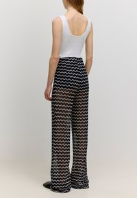 Witte mouwloze top gecombineerd met marineblauwe sheer broek met zigzagpatroon, met een losse pasvorm en flared pijpen. Zwarte schoenen maken de look compleet.