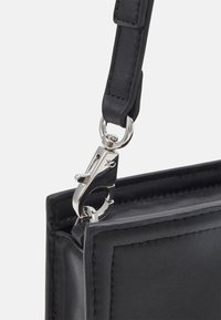 Angolo di una borsa in pelle nera con una chiusura in metallo argento. Texture liscia, linee pulite e dettagli di cucitura minimi.