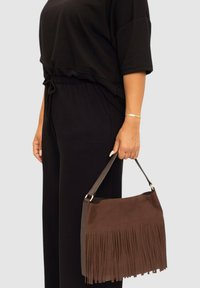 Bolso de hombro de cuero marrón con detalles de flecos. Presenta un acabado suave, herrajes en tono dorado y una forma estructurada.