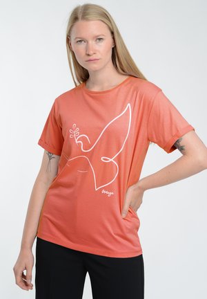 Koralfarvet T-shirt med korte ærmer, udsmykket med et hvidt abstrakt fuglemotiv, glat tekstur og afslappet pasform, parret med sorte bukser.