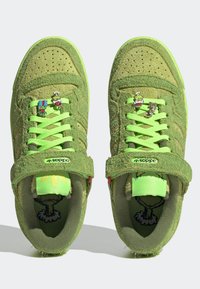 Dětské zelené chlupaté tenisky Adidas s ozdobami na tkaničkách v podobě kreslených postaviček a suchými zipy, pohled shora na bílém pozadí.