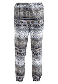 Pantalon ample avec taille et poignets élastiques, présentant des motifs tribaux et géométriques horizontaux en gris, noir, blanc, bleu et marron.