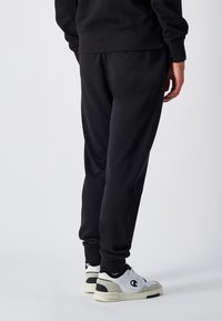 Svarte joggebukser lavet af en bomuldsblanding, med en tapered pasform og elastisk talje. Blandet med hvide Champion sneakers.