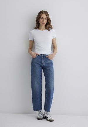 Weißes, eng anliegendes Kurzarm-T-Shirt, kombiniert mit hochtaillierten, geraden blauen Jeans und weißen Sneakers mit schwarzen Streifen. Glatte Textur.