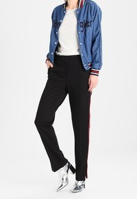 Modrá denimová bomber bunda s černým nápisem, bílý tričko, černé elegantní kalhoty s červenými bočními pruhy, metalické stříbrné kotníčkové boty.