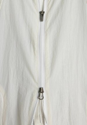 Tessuto di abbigliamento bianco con primo piano di una zip argento bidirezionale parzialmente aperta.