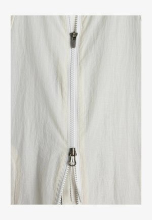 Tessuto di abbigliamento bianco con primo piano di una zip argento bidirezionale parzialmente aperta.