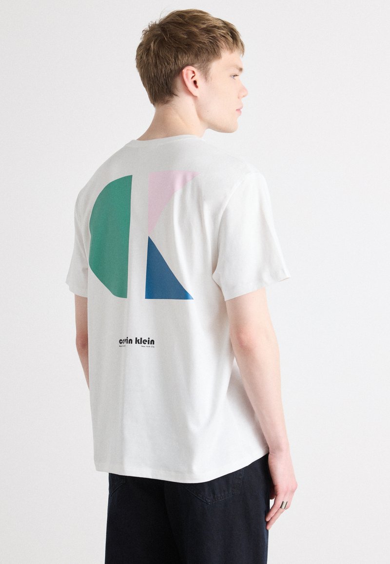 Balta medvilninė marškinėliai su geometriniu raštu ant nugaros, kuriame matomi mėlyni, žali ir rožiniai formos, o po jais išspausdinta "calvin klein" juoda spalva.