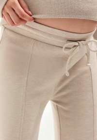 Beige, weiche Joggings mit einem elastischen Bund, vorderem Kordelzug und seitlichen Nähten. Sichtbare gerippte Details an der Taille.