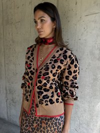 Sweter w wzór panterki w odcieniach brązu, czerni i czerwonych akcentach. Posiada ściągacze przy mankietach i u dołu, duże guziki z przodu oraz dopasowaną spódnicę w wzór panterki.