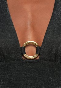 Black garment featuring a deep V-neck with a gold hardware ring detail, accentuated by textured fabric with subtle shimmer.