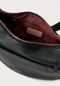 Sac à main en cuir noir avec une finition texturée, une fermeture éclair dorée et une doublure en tissu marron foncé. Contient une étiquette indiquant "Cuir italien authentique."