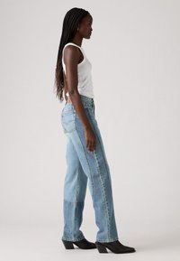 Jeans in denim blu chiaro con una vestibilità comoda e texture sbiadita, dotati di un'etichetta sul retro e cuciture a contrasto, abbinati a una canotta bianca e stivali neri con tacco.