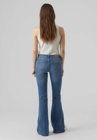 Laienevad sinised denim püksid keskmise pesuga, viie tasku ja kontrastsete õmblustega. Ülal on pehme valge top.