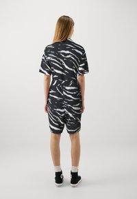 Un combishort à rayures zèbre noir et blanc avec une coupe ample, des manches courtes et une taille cintrée. Porté avec des chaussures montantes noires.