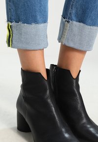 Botines de cuero negro con un acabado texturizado, con un tacón bajo y una cremallera lateral. Jeans con puños doblados que muestran acentos de costura amarilla.
