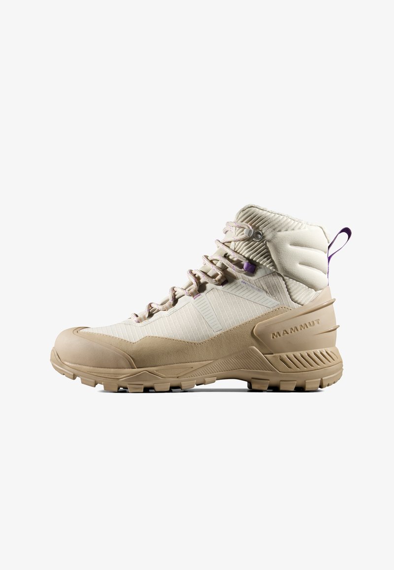 Beżowy but turystyczny z teksturowaną cholewką, wzmocnionym noskiem i wyściełanym kołnierzem. Posiada fioletowe akcenty oraz solidną podeszwę zapewniającą przyczepność.