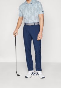Polo bleu clair avec motif en losanges, pantalon bleu marine, ceinture grise et chaussures de sport blanches avec des accents bleus ; golfeur tenant un club.