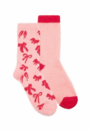 Pair of soft pink fuzzy socks, one with red bow patterns, the other plain with red toe and cuff accents.