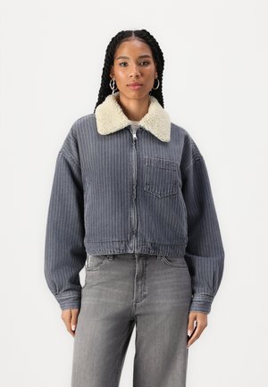 Veste en denim courte de couleur bleu foncé avec des rayures verticales blanches, dotée d'un col en fourrure de couleur crème et d'une poche avant.