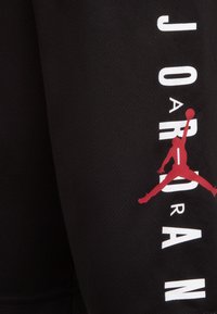 Black athletic shorts featuring textured fabric, a large red Jumpman logo, and white "JORDAN" lettering on the side.