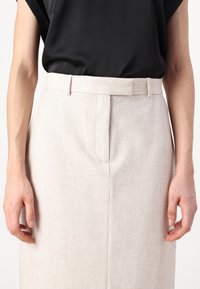 Světle béžové kalhoty na míru s texturovanou tkaninou, se záhybem na přední straně a slim fit, v kombinaci s černým topem s krátkým rukávem.