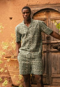 Groen shirt met korte mouwen en bijpassende shorts met een geometrisch bladerenpatroon. Gemaakt van lichtgewicht stof, met knopen en een notch-kraag.